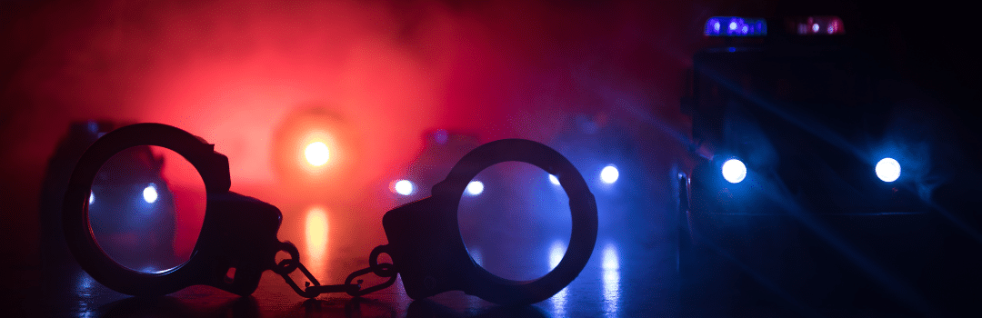 handcuffs on pavement at night with police cars in background