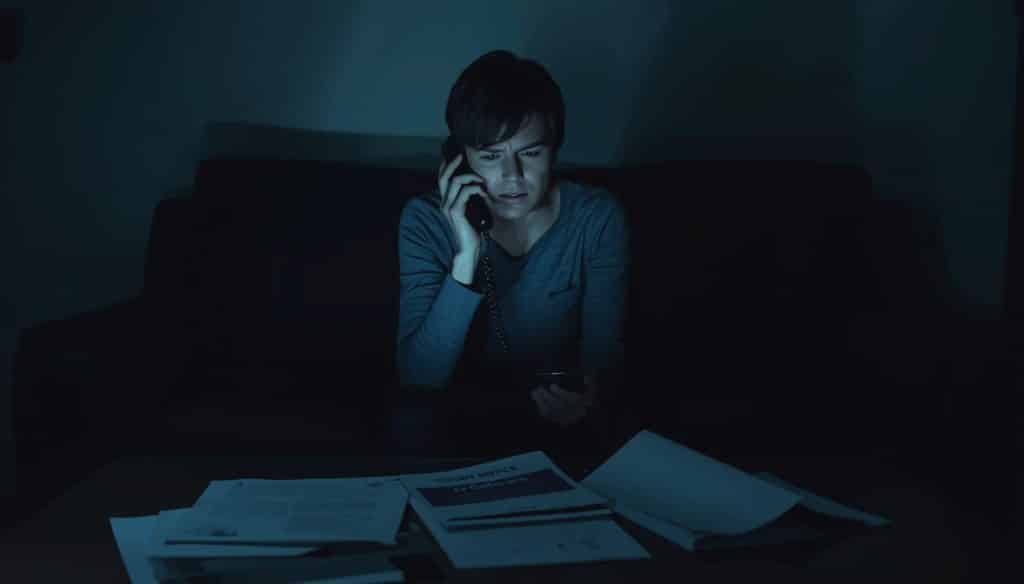 A distressed person sitting on a couch in a dark room, talking on a phone with "Court Notice" papers on the table.
